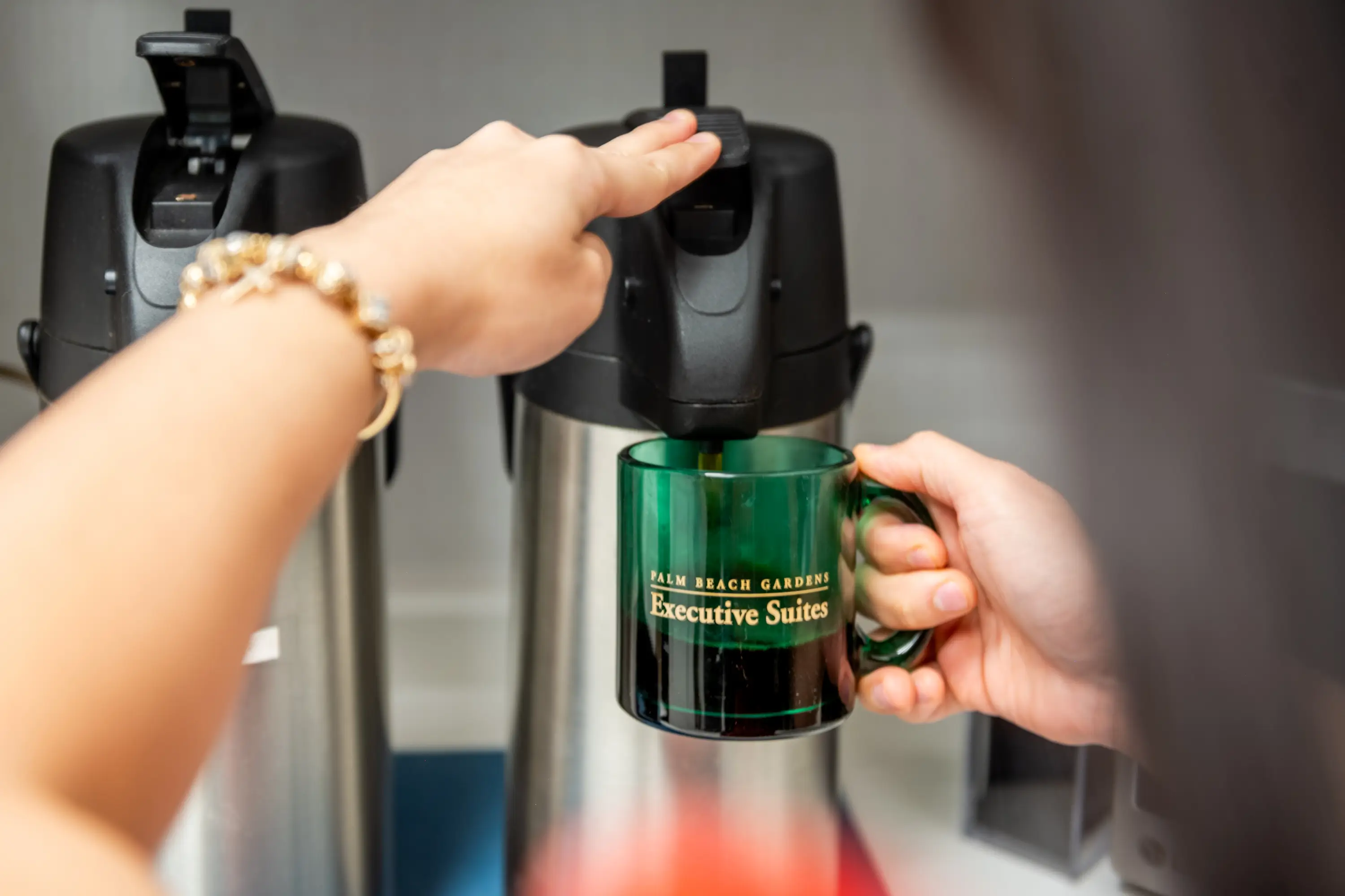 A person holding a coffee mug over a coffee pot.