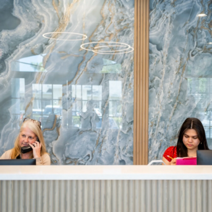 Two women sitting at a counter in front of a marble wall.